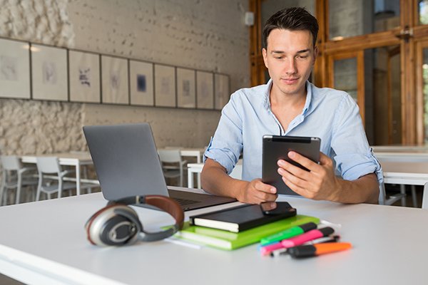 young hadsome busy man concentrated on work in laptop, holding tablet computer, confident andd successful
